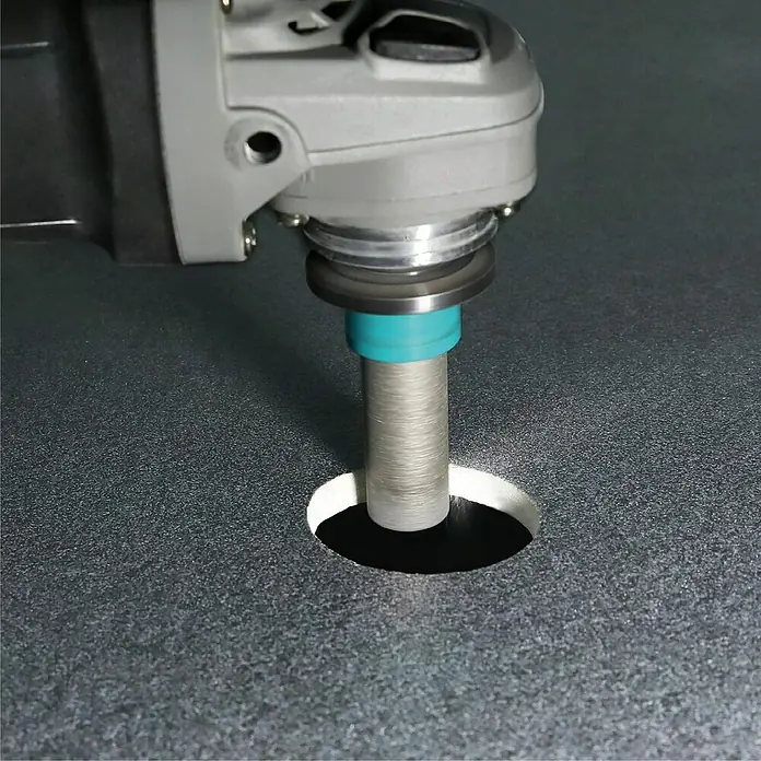 Bihui Hohlbohrkrone DMB - Durchmesser: 20 mm, Geeignet für: Keramik - Winkelschleifer mit metallischem Kernbohrer mit türkisfarbenem Ring, der ein sauberes Loch in eine dunkle, strukturierte Oberfläche schneidet.