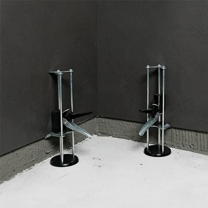 Bihui Fliesenheber TAS25 - Tragkraft: 160 kg, 2 Stk. - Zwei metallisch-schwarze verstellbare Eckhalterungen stützen dunkelgraue Platten in einer Ecke.