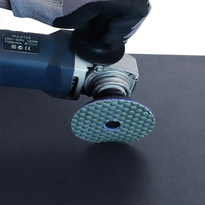 Bihui Diamant-Schleifteller DPP405 - Körnung: 50, Durchmesser: 100 mm - Hand hält Winkelschleifer mit sechseckiger Polierscheibe, die auf einer dunklen Oberfläche arbeitet.