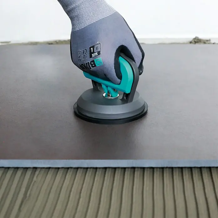 Bihui Saugheber SCSP4 - Tragkraft: 35 kg - Behandschuhte Hand positioniert mit grau-türkisem Saugnapf-Werkzeug eine dunkle Fliese auf geripptem Kleber.