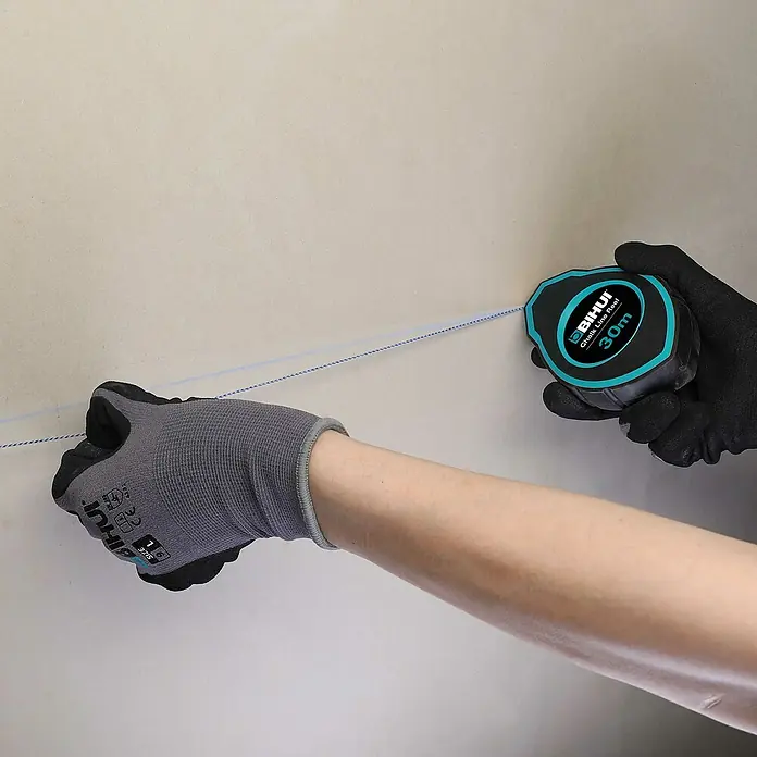 Bihui Schlagschnurpuder CTCAKK2 - Länge Schnur: 30 m - Behandschuhte Hände verwenden eine schwarz-türkise BIHUI 30m Schlagschnurrolle, um eine blaue Linie auf einer hellen Wand zu markieren.