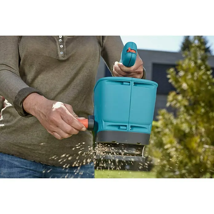 Gardena Handstreuer M - Streubreite: 1 m - 4 m, 1,8 l - Ein Gärtner benutzt einen Gardena Streuwagen, um Samen auszubringen. Das Gerät ist blau und wird mit der Hand bedient.