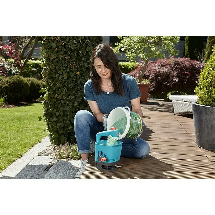 Gardena Handstreuer M - Streubreite: 1 m - 4 m, 1,8 l - Frau befüllt einen Gardena Streuwagen mit Dünger, um ihren Garten optimal zu pflegen und zu düngen.