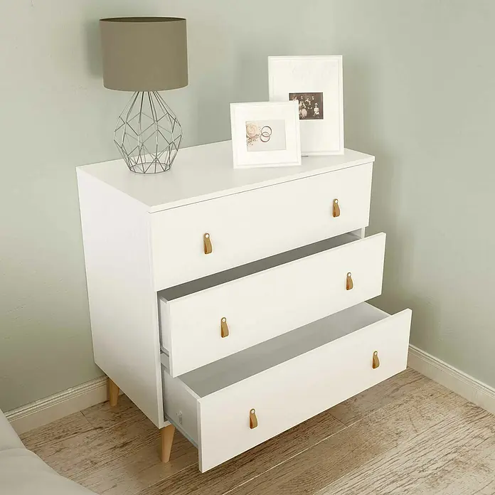 Meka Block Cómoda K-690 - L x An x Al: 48 x 80 x 83,5 cm, Blanco poro, Número de cajones: 3 ud. - Cómoda blanca con tres cajones y tiradores de cuero, coronada con una lámpara y marcos de fotos, con algunos cajones parcialmente abiertos.