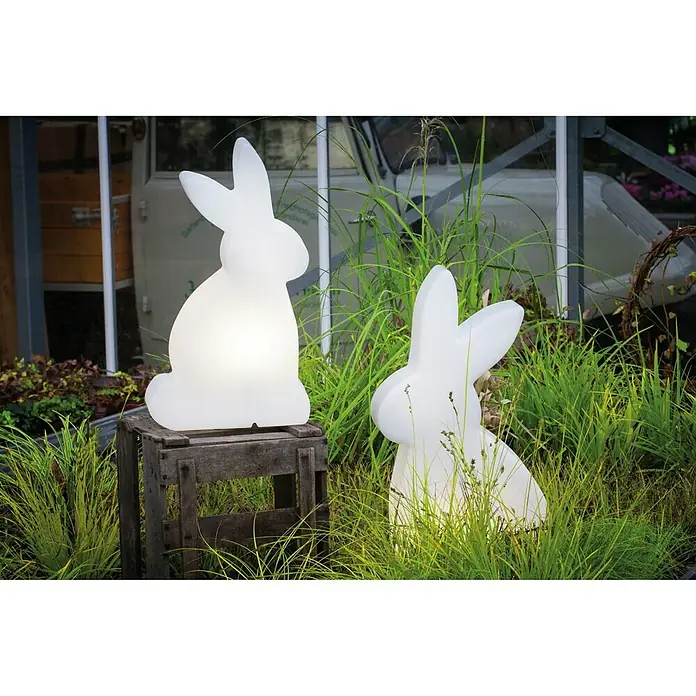 8 Seasons Design Shining Dekoleuchte Rabbit - 9 W, Weiß, L x B x H: 16 x 45 x 79 cm - Zwei leuchtende Hasenfiguren, eine auf einer Holzkiste, umgeben von Gras, die als dekorative Gartenbeleuchtung dienen.