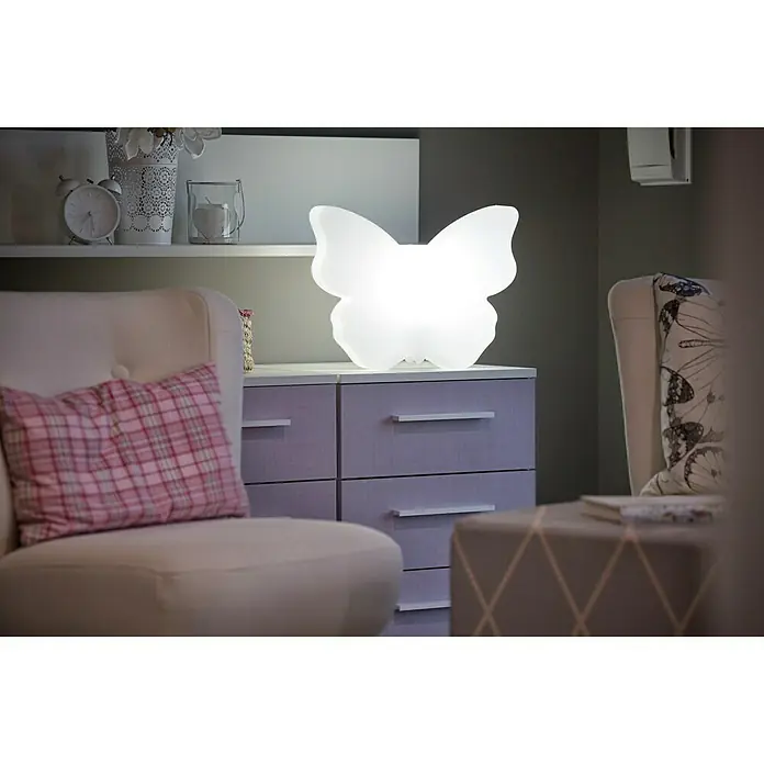 8 Seasons Design Shining Dekoleuchte Butterfly - 9 W, Weiß, L x B x H: 10 x 40 x 32 cm - Eine Nahaufnahme einer Nachttischlampe in Form eines Schmetterlings auf einer Kommode, die ein sanftes, warmes Licht ausstrahlt.