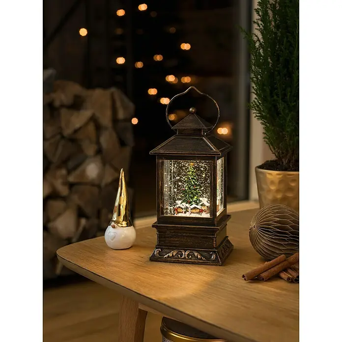 Konstsmide LED-Schneelaterne Weihnachtsmarkt - Innen, Braun, 10,5 x 10,5 x 22 cm, Batteriebetrieben - Weihnachtliche Schneekugellaterne mit Tannenbaum und Häusern auf einem Holztisch mit Dekorationen.