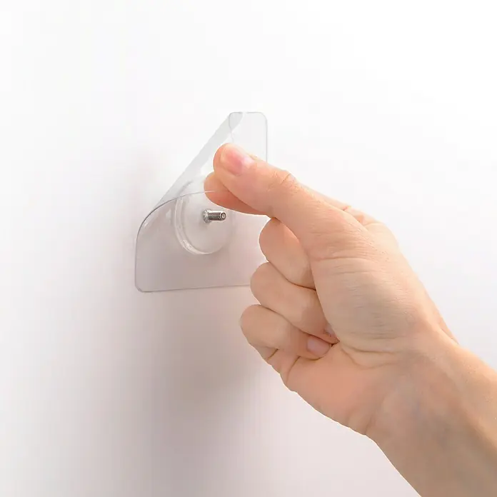 Tatay Kit de fijación Quick Fix - Transparente - Primer plano de un gancho adhesivo transparente con una mano, montado en una pared blanca, que muestra su funcionalidad y facilidad de instalación.