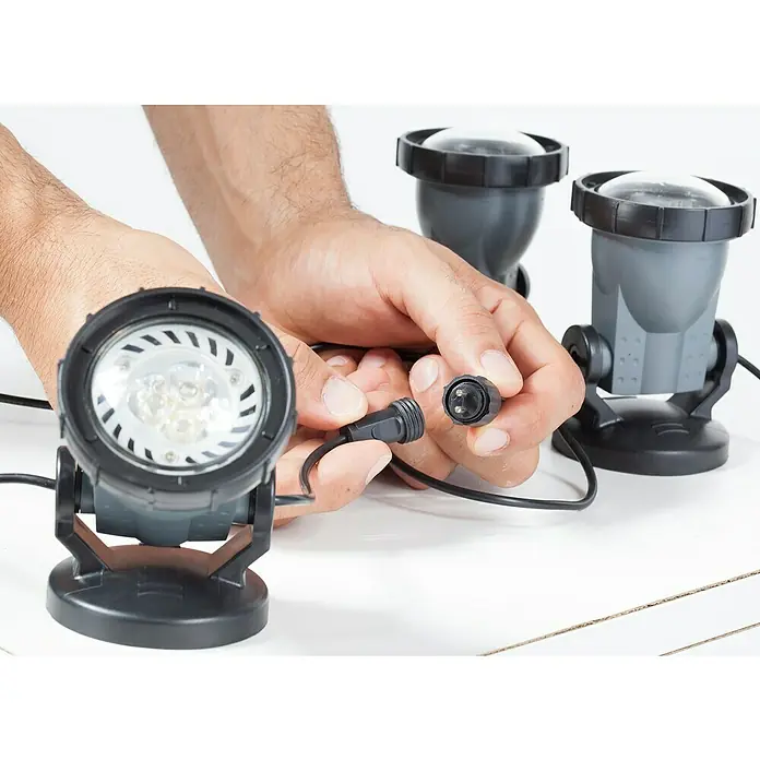 Heissner Teichbeleuchtung - 4,5 W, Warmweiß - Hände verbinden einen schwarzen wasserdichten Stecker mit einem grauen LED-Strahler mit klarer Linse, zwei weitere Strahler im Hintergrund.