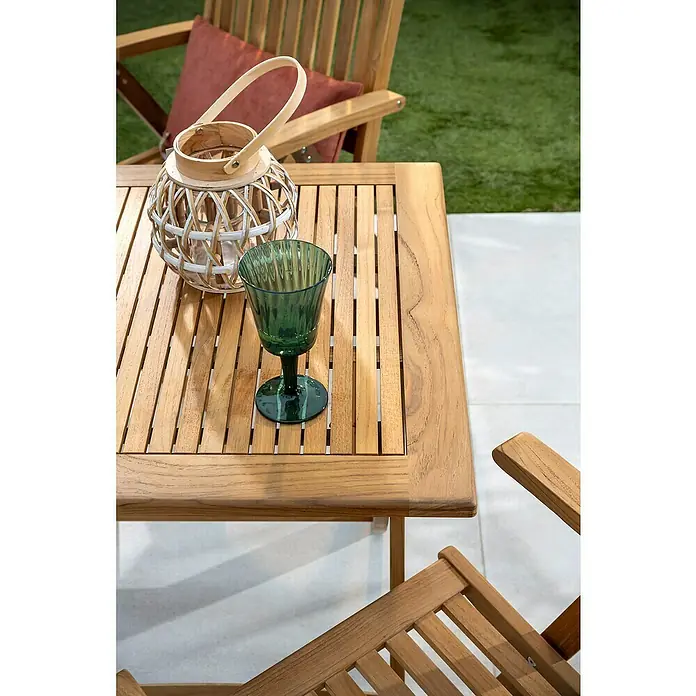 Mesa de jardín Zaira - L x An x Al: 70 x 70 x 74 cm, Teca, Natural, Abatible - Primer plano de una mesa de madera con un vaso verde y una linterna decorativa al aire libre. La mesa está formada por listones de madera.