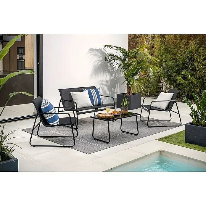 Sunfun Conjunto de muebles Deia - 4 pzs., Textiline/Acero, Antracita - Un elegante conjunto de patio con estructuras de metal negro, que incluye un sofá, sillas y mesa, complementado con vegetación y una piscina.