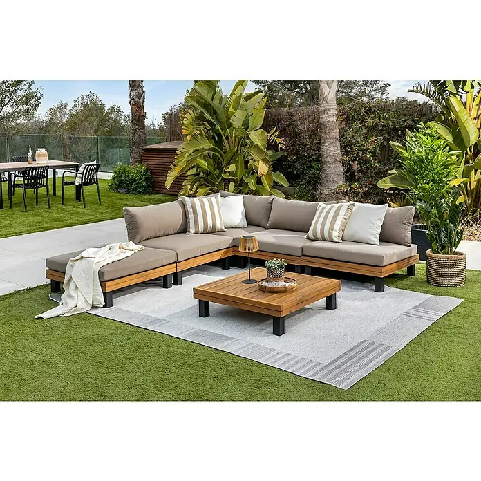 Conjunto de muebles Elsa - 6 pzs., Madera de acacia/Aluminio, Marrón - Un elegante conjunto de salón de exterior con mesa de centro sobre una alfombra gris, rodeado de exuberante vegetación. Perfecto para relajarse al aire libre.