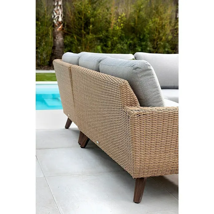 Conjunto de muebles Royal sofá esquinero + mesa - 2 pzs., Ratán sintético/Aluminio, Beige - Primer plano de un sofá de exterior de ratán con cojines grises y patas de madera, situado en un patio con una piscina al fondo.