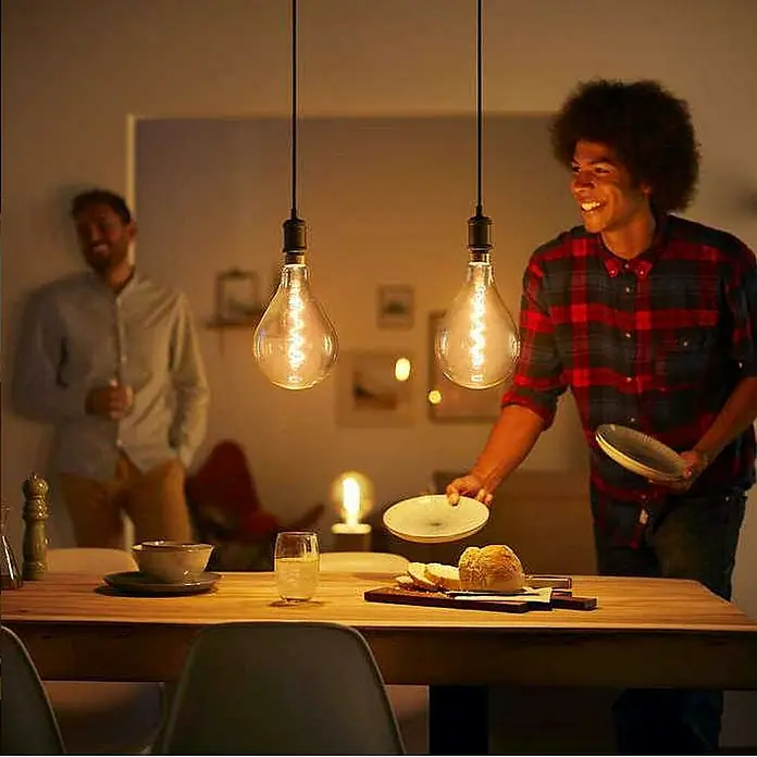 Philips Lámpara colgante LED Estándar - 40 W, L x An x Al: 7,1 x 16,9 x 16,9 cm, Negro, E27 - Dos bombillas Edison decorativas cuelgan sobre una mesa de comedor, iluminando una reunión social con luz cálida.