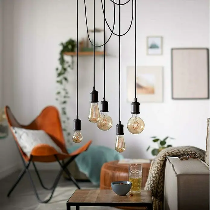 Philips Lámpara colgante LED Estándar - 40 W, L x An x Al: 7,1 x 16,9 x 16,9 cm, Negro, E27 - Primer plano de múltiples bombillas Edison colgando del techo con una sala de estar moderna al fondo.