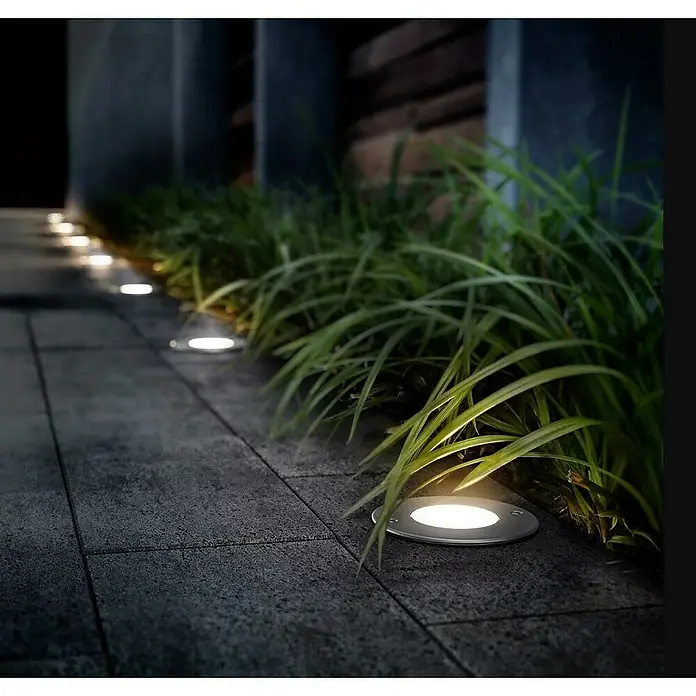 Philips Foco LED empotrable exterior Moss - 3 W, L x An: 10,5 x 10,5 cm, Blanco cálido, Acero inoxidable - Fila de luces de suelo a lo largo de un sendero pavimentado con exuberante vegetación, creando iluminación ambiental exterior y seguridad.
