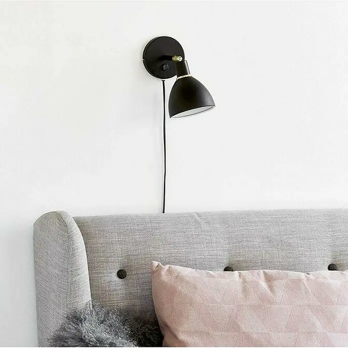 Nordlux Ray Aplique de pared - 40 W, L x An x Al: 12 x 12 x 20 cm, Negro, E14 - Lámpara de pared negra con pantalla ajustable sobre un cabecero gris con cojín rosa. El diseño es moderno y elegante.