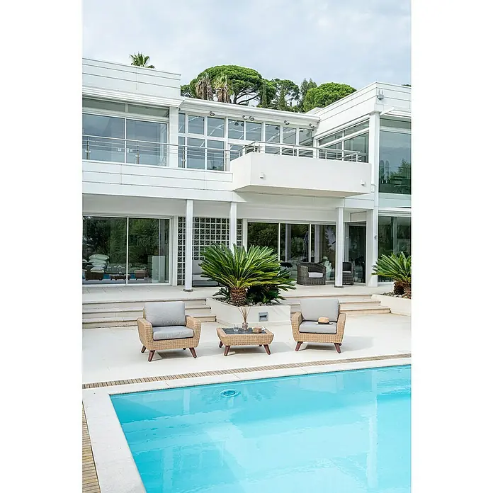 Conjunto de muebles Royal sillones + mesa - 3 pzs., Ratán sintético/Aluminio, Beige - Diseño moderno de patio con sillones de mimbre, una mesa y una piscina frente a un elegante edificio blanco. Ambiente relajante al aire libre.