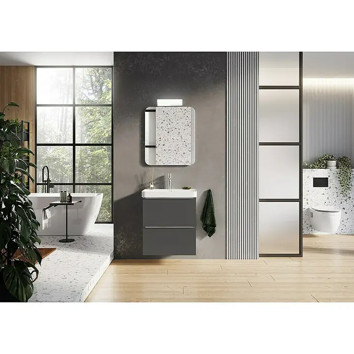 Riva Beauty 2.0 Waschtischunterschrank - B x T x H: 58,5 x 43,7 x 63,5 cm, Anthrazit - Badezimmer mit modernem Waschtisch in Grau, Spiegel mit Terrazzo-Muster und freistehender Badewanne vor großem Fenster mit Blick ins Grüne.