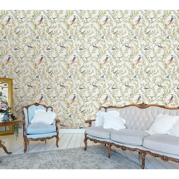 Glööckler Pompöös Provence Vliestapete - Grau/Grün/Rot, Floral, 10,05 x 0,53 m - Raumansicht mit einem blassblauen Sessel und einem grauen Sofa, beide mit aufwendigen Holzrahmen, vor einer lebhaften Vogel- und Blumenmustertapete.