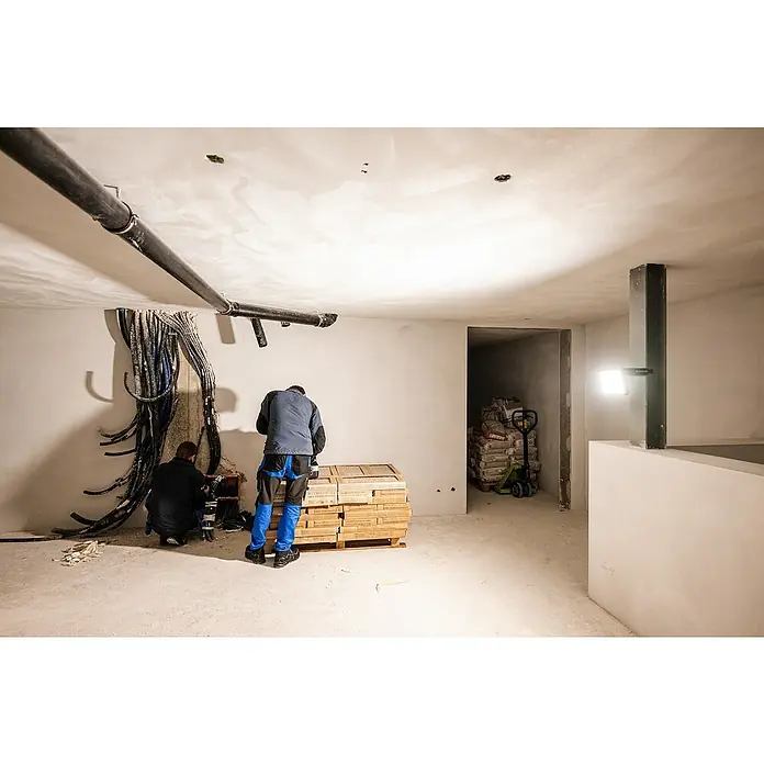Ledlenser LED Baustrahler AF8R WORK - 4.000 lm, 3.000 K - 6.500 K, 4,1 x 27,5 x 17,9 cm, IP67 - Arbeiter bereiten einen unfertigen Raum mit Sanitäranlagen, Elektroleitungen und Stapeln von Feinsteinzeugfliesen vor.