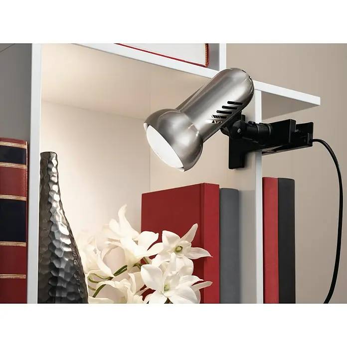 Eglo Klemmleuchte Manhatten - 60 W, Farbe Gehäuse: Nickel matt - Eine silberne Klemmlampe beleuchtet Bücher und Dekorationen in einem weißen Regal, perfekt für Akzentbeleuchtung.