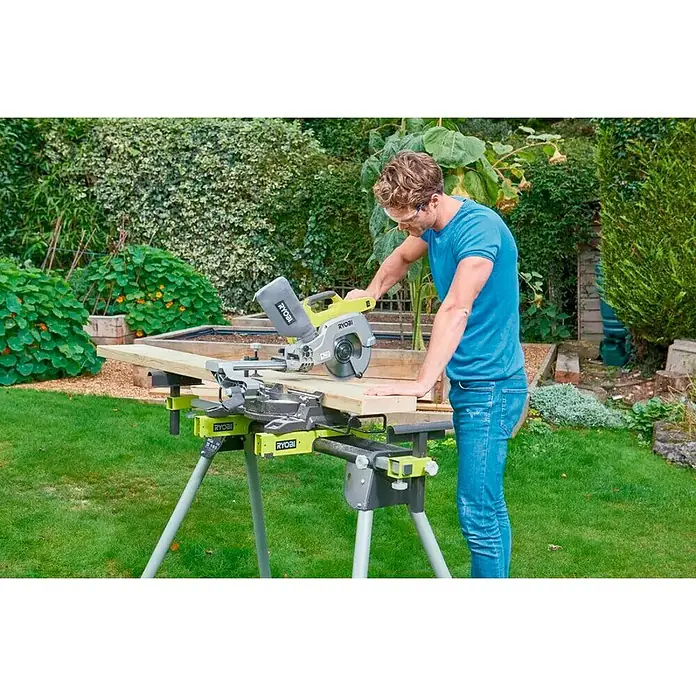 Ryobi ONE+ Akku-Kapp- & Gehrungssäge R18MS216-0 - 18 V, Li-Ionen, Ohne Akku, 0 U/min - 3.200 U/min - Eine Ryobi Kapp- und Gehrungssäge schneidet ein Holzbrett auf einem klappbaren Ständer im Freien.