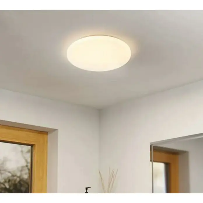 Eglo Plafón LED redondo Pogliola-E - 15,6 W, Ø x Al: 31 x 5,5 cm, Blanco, Efecto cristal, Blanco neutro - Una lámpara de techo redonda emite una luz brillante y cálida en una habitación decorada modernamente con paredes blancas y detalles en madera.