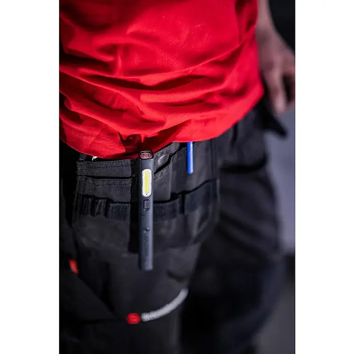 Ledlenser LED-Arbeitsleuchte Stiftleuchte W2R Work - 160 lm, Lichtfarbe: Kaltweiß, IP54 - Schwarze Arbeitsleuchte mit weißem LED-Streifen, in die Tasche einer dunklen Arbeitshose geklemmt, getragen von einer Person in rotem Shirt.