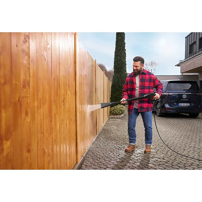 Kärcher Strahlrohr eco!Booster 120 - Passend für: Kärcher Hochdruckreiniger K 2 und K 3, 452 x 104 x 42 mm - Ein Mann reinigt einen Holzzaun mit einem schwarzen Hochdruckreiniger, Wasser sprühend.