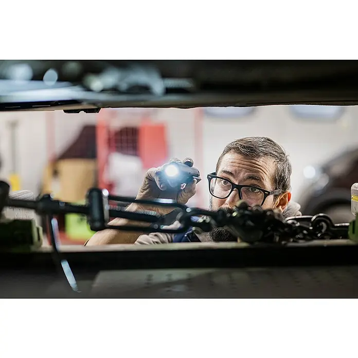 Ledlenser LED-Arbeitsleuchte W5R Work - 600 lm, Lichtfarbe: Kaltweiß, IP54 - Mann mit Brille und Bart inspiziert eine Maschine mit einer hellen Taschenlampe.