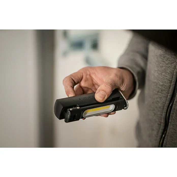 Ledlenser LED-Arbeitsleuchte W6R Work - 500 lm - 600 lm, Lichtfarbe: Kaltweiß, IP54 - Hand hält eine kompakte schwarze Arbeitsleuchte mit einem leuchtend gelben LED-Streifen.