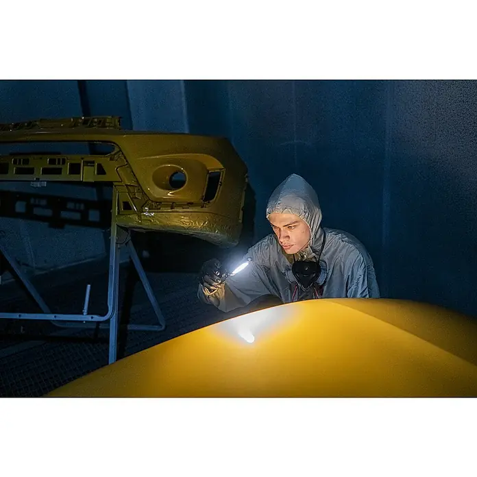 Ledlenser LED-Arbeitsleuchte W7R Work - 600 lm, Lichtfarbe: Kaltweiß, IP54 - Person in Schutzkleidung inspiziert gelbes Autoteil mit Taschenlampe.