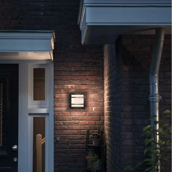 Philips Aplique exterior LED Petronia - 12 W, 53 x 190 x 190 mm, Antracita, Blanco, IP44 - Luz exterior cuadrada en una pared de ladrillos, que emite un brillo cálido y crea un ambiente acogedor.