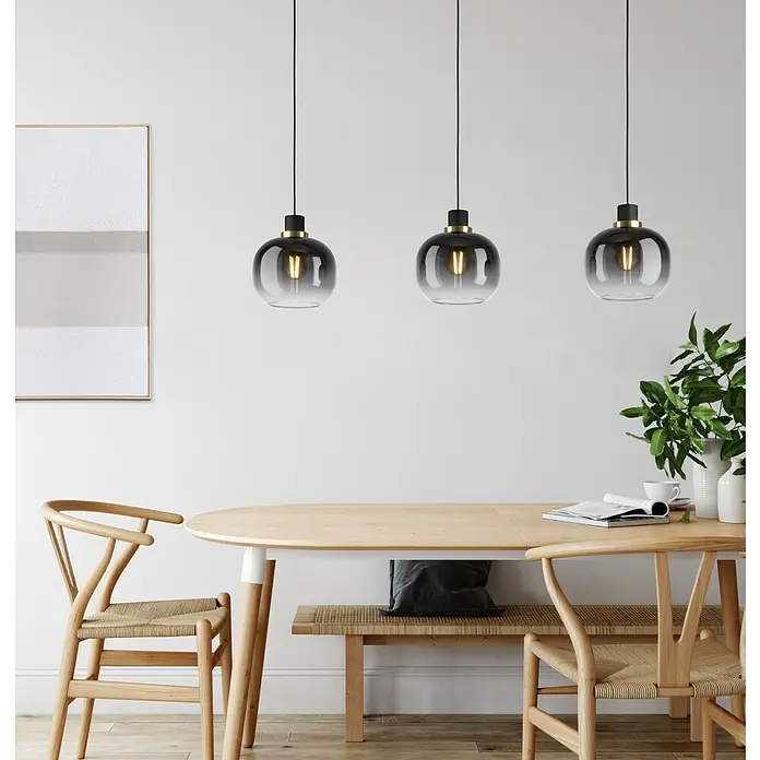 Eglo Pendelleuchte OILELLA - 40 W, L x B x H: 95 x 19 x 110 cm, Schwarz/Messing, E27 - Drei stilvolle Hängeleuchten mit rauchgrauen Glasschirmen und warmen Glühbirnen über einem Esstisch, der eine gemütliche Atmosphäre schafft.