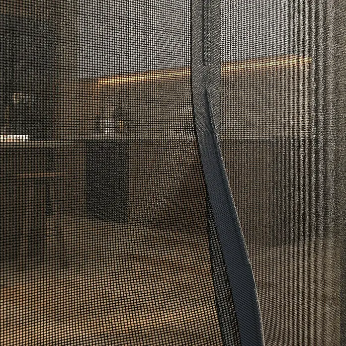 Easy Life Insektenschutz-Magnetrahmen - B x H: 100 x 220 cm, Farbe Netz: Anthrazit, Art Verschluss: Magnetverschluss - Nahaufnahme eines schwarzen Insektenschutzgitters, das einen unscharfen Blick auf einen Innenraum mit warmen Licht bietet. Das Netz ist fein und strukturiert.