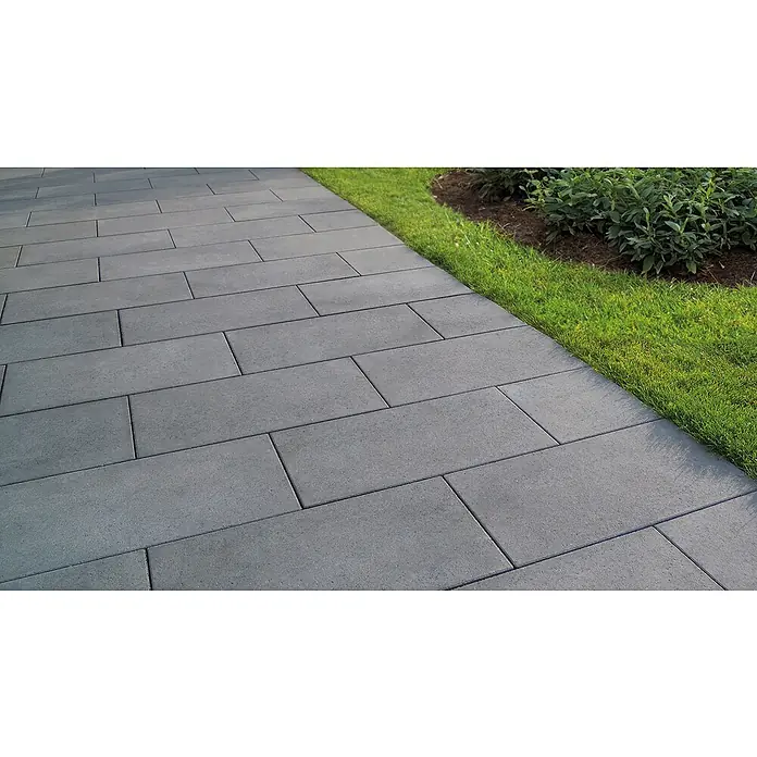 EHL Pflasterstein Cortona - Anthrazit, 60 x 30 x 8 cm, Rechteckig - Nahaufnahme eines gepflasterten Weges mit grauen Pflastersteinen, der von saftigem Gras und üppigen Pflanzen gesäumt ist.
