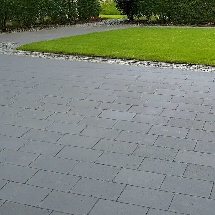 EHL Pflasterstein Cortona - Anthrazit, 60 x 30 x 8 cm, Rechteckig - Ansicht eines mit grauen Pflastersteinen ausgelegten Außenbereichs, umgeben von Grünflächen und Büschen, die eine gepflegte Atmosphäre schaffen.