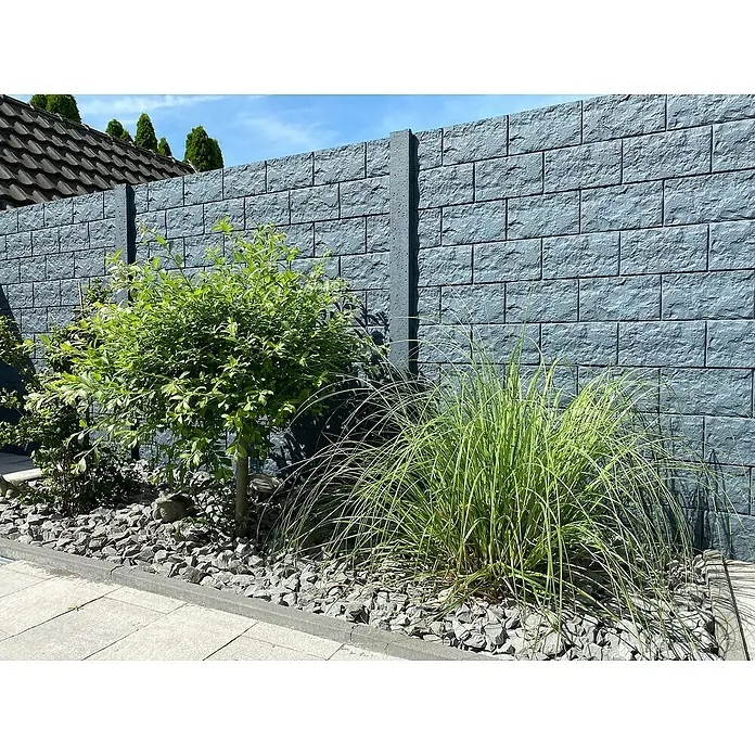 Beckers Betonzaun Zaunelement Standard Casa Borsika - 200 x 38,5 cm, Beton, Betongrau - Eine graue Steinmauer mit Pflanzen davor, die eine ruhige Gartenszene schafft. Die Textur der Mauer harmoniert gut mit dem Grün der Pflanzen.