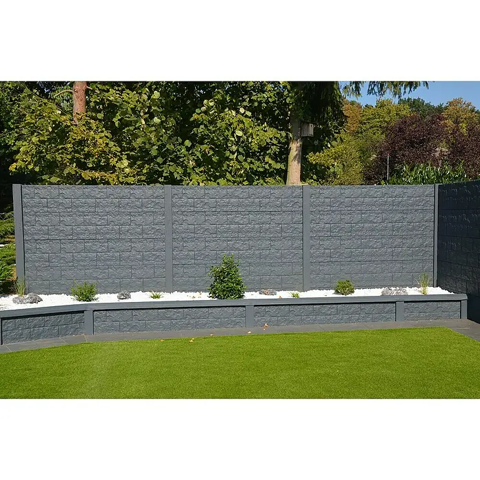 Beckers Betonzaun Zaunelement Standard Casa Borsika - 200 x 38,5 cm, Beton, Betongrau - Eine graue Steinmauer mit kleinen Pflanzen und weißen Kieselsteinen vor üppigem Grün.