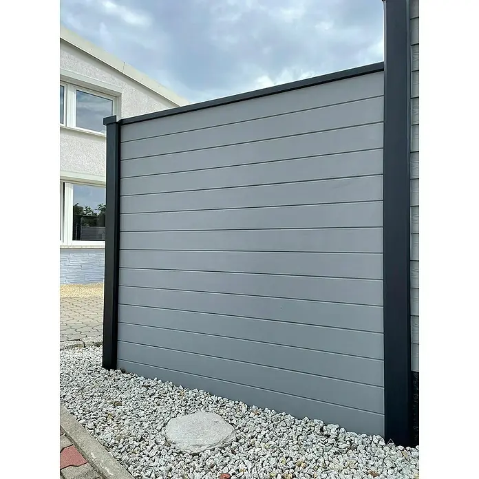Beckers Betonzaun Zaunelement Prestige Glatt Motiv - 184 x 26 cm, Beton, Betongrau - Diese Nahaufnahme zeigt einen modernen, grauen Sichtschutzzaun mit horizontalen Paneelen und schwarzen Rahmenpfosten. Der Zaun steht auf weißen Zierkieseln.