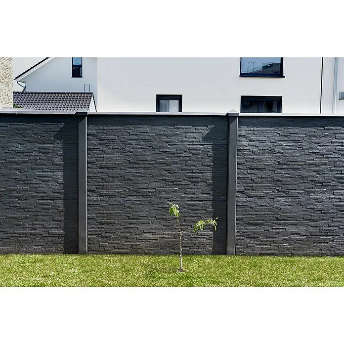 Beckers Betonzaun Zaunelement Klassik Rimini Motiv - 184 x 26 cm, Beton, Betongrau - Eine stilvolle, dunkle Steinmauer mit dekorativen Säulen und einem kleinen Baum davor. Die Mauer verleiht dem Garten Struktur.