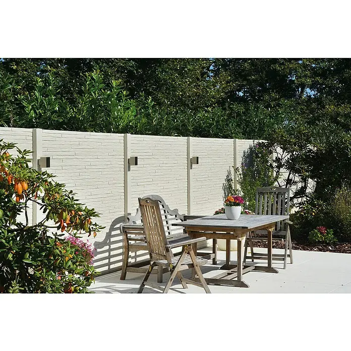 Beckers Betonzaun Zaunelement Standard Toscana Motiv - 200 x 38,5 cm, Beton, Betongrau - Außenaufnahme einer Terrasse mit Gartenzaun, Holztisch und Stühlen, üppigem Grün und dezenten Wandleuchten.