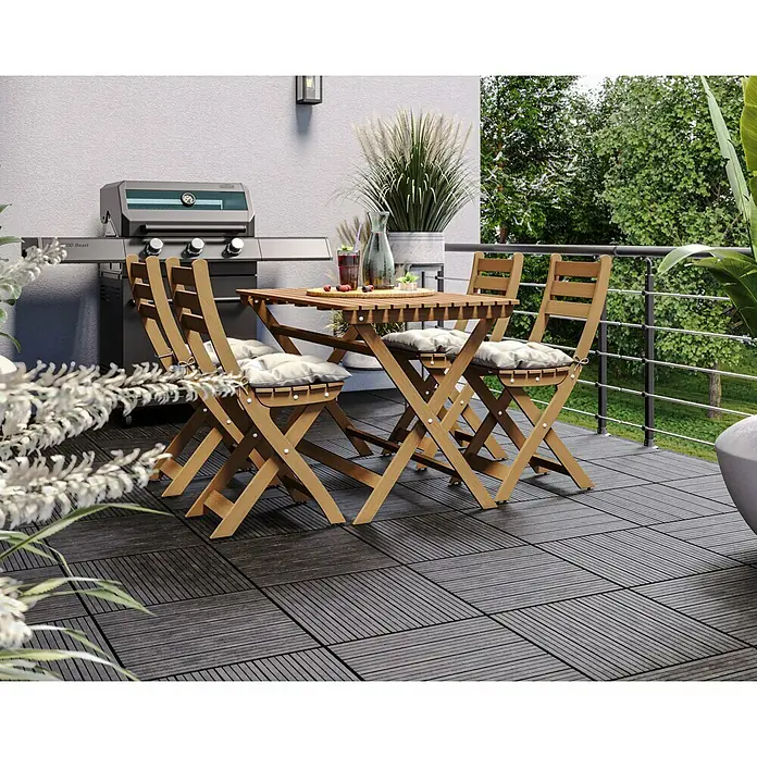 Klickfliese Cosmopolitan - Kunststoff, 45 x 45 x 2,5 cm, Stahlgrau, 1 Stk. - Gartentischgruppe mit Holztisch und Stühlen mit grauen Sitzkissen auf einer Terrasse mit Grill.