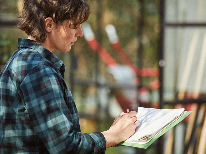 Frau steht im Garten und schreibt auf einem Blatt Papier etwas auf