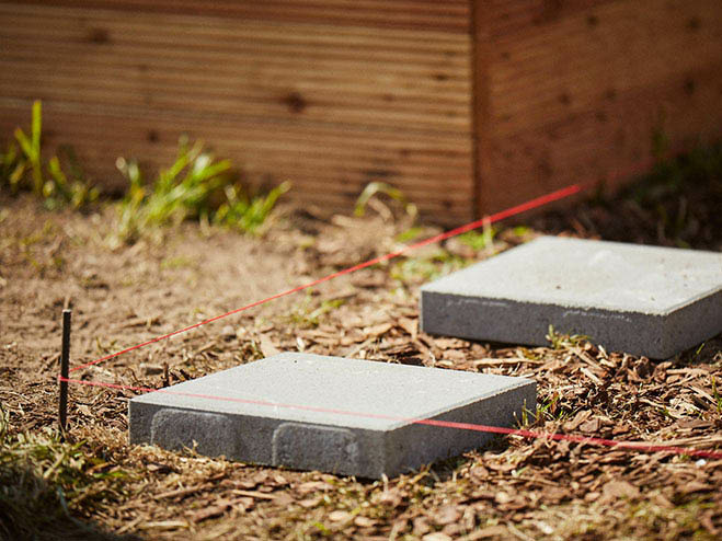 Betonplatten liegen am Boden im Garten als Untergrund für den Holzweg