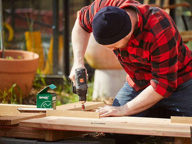 Mann verschraubt die Terrassendielen im Garten