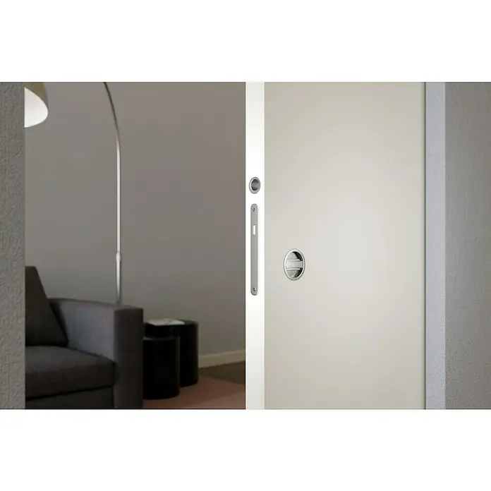 Entravia Holzschiebetür - 985 x 1.985 mm, CPL, Weiß ähnlich RAL 9016, Mit Schlossfräsung, Passend für: Entravia Simple-Pocket Schiebetürsystem - Silberner Muschelgriff und Schloss für Schiebetüren an einer weißen Tür, leicht geöffnet zu einem modernen Wohnzimmer.
