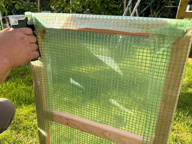 Grüne Gewächshausfolie wird an das selbstgebaute Fenster aus Holz angetackert