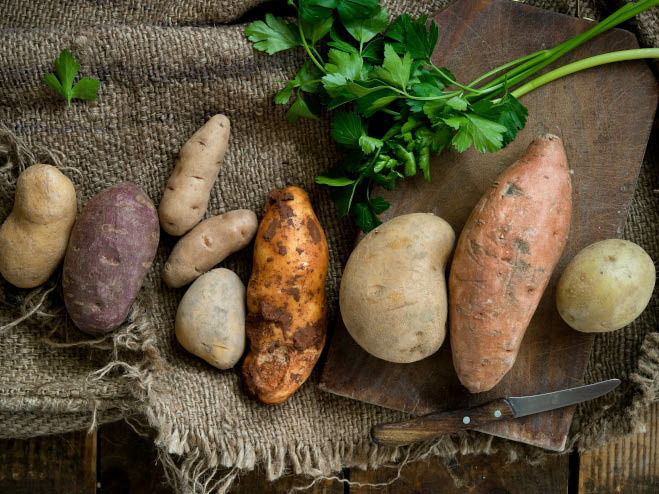 Verschiedene Kartoffeln liegen auf Leinensack, daneben Kräuter